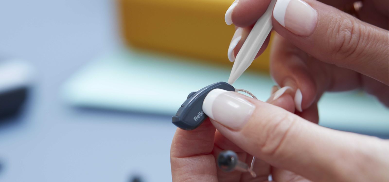 Person holding a hearing aid and using a tool to clean it.