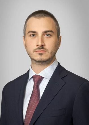 A man in a suit and tie is standing in front of a white background.