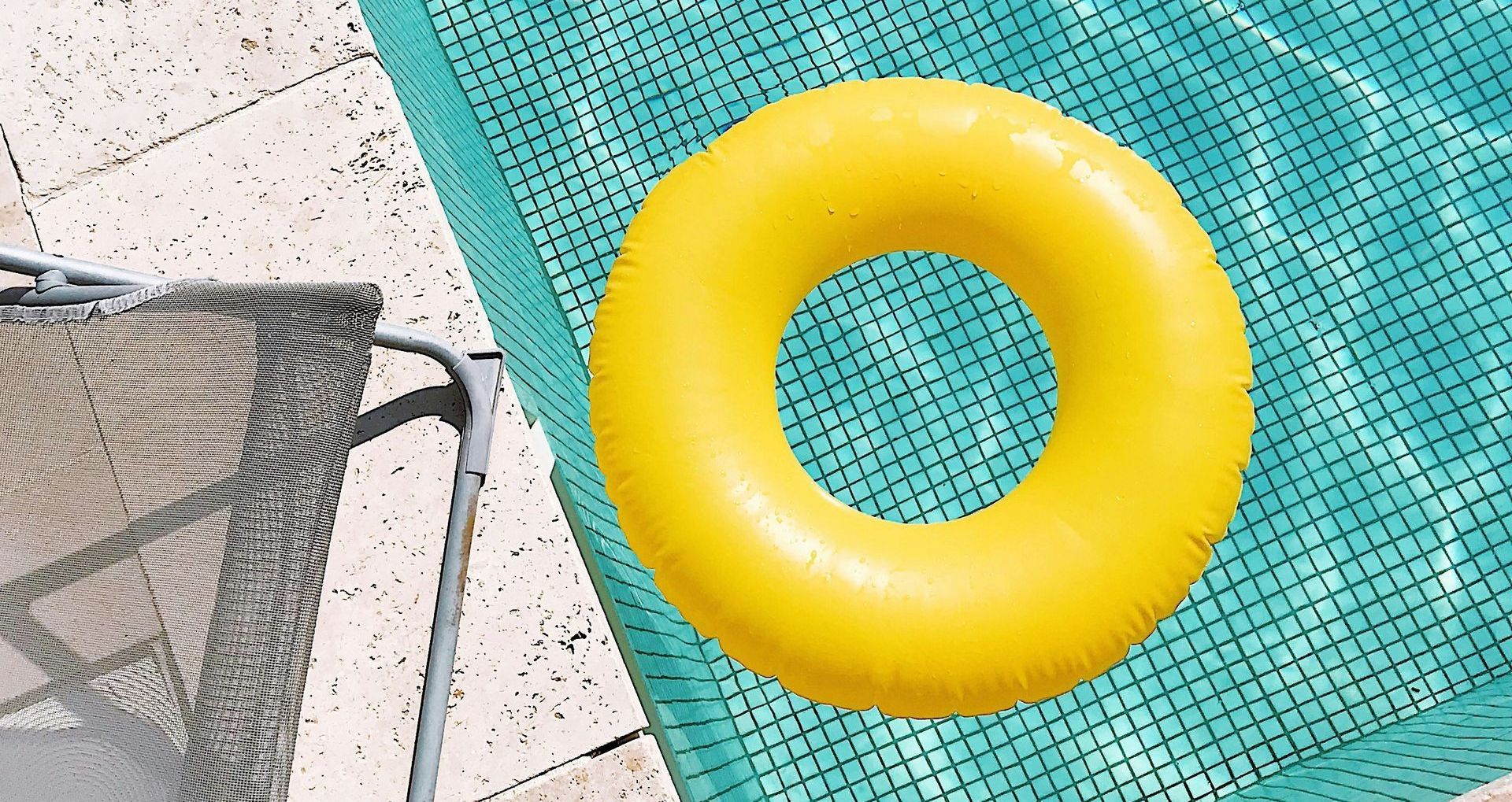A yellow life preserver is floating in a swimming pool next to a chair.