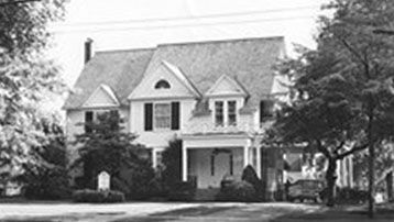 A black and white photo of a large house surrounded by trees.