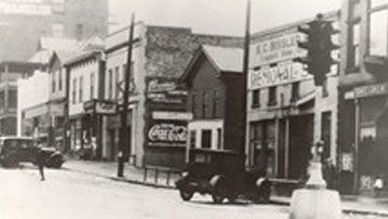 A black and white photo of a city street with a car parked on the side of the road.