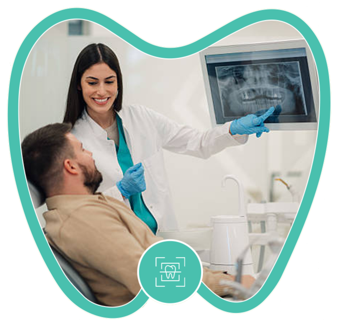 A dentist pointing to a dental X-ray on a screen while consulting with a patient in a clinical setting.