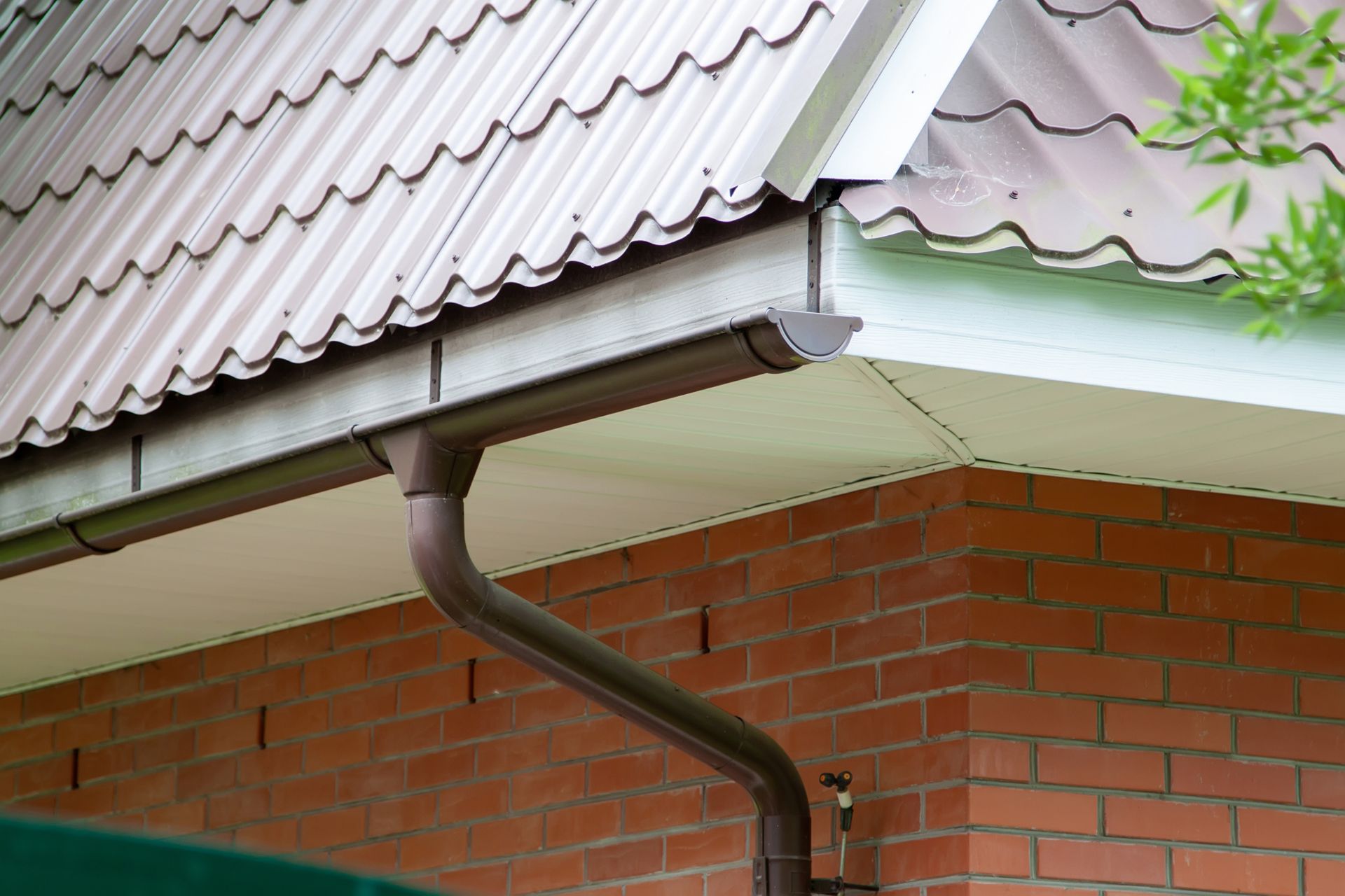 A brown gutter is attached to the side of a brick building.