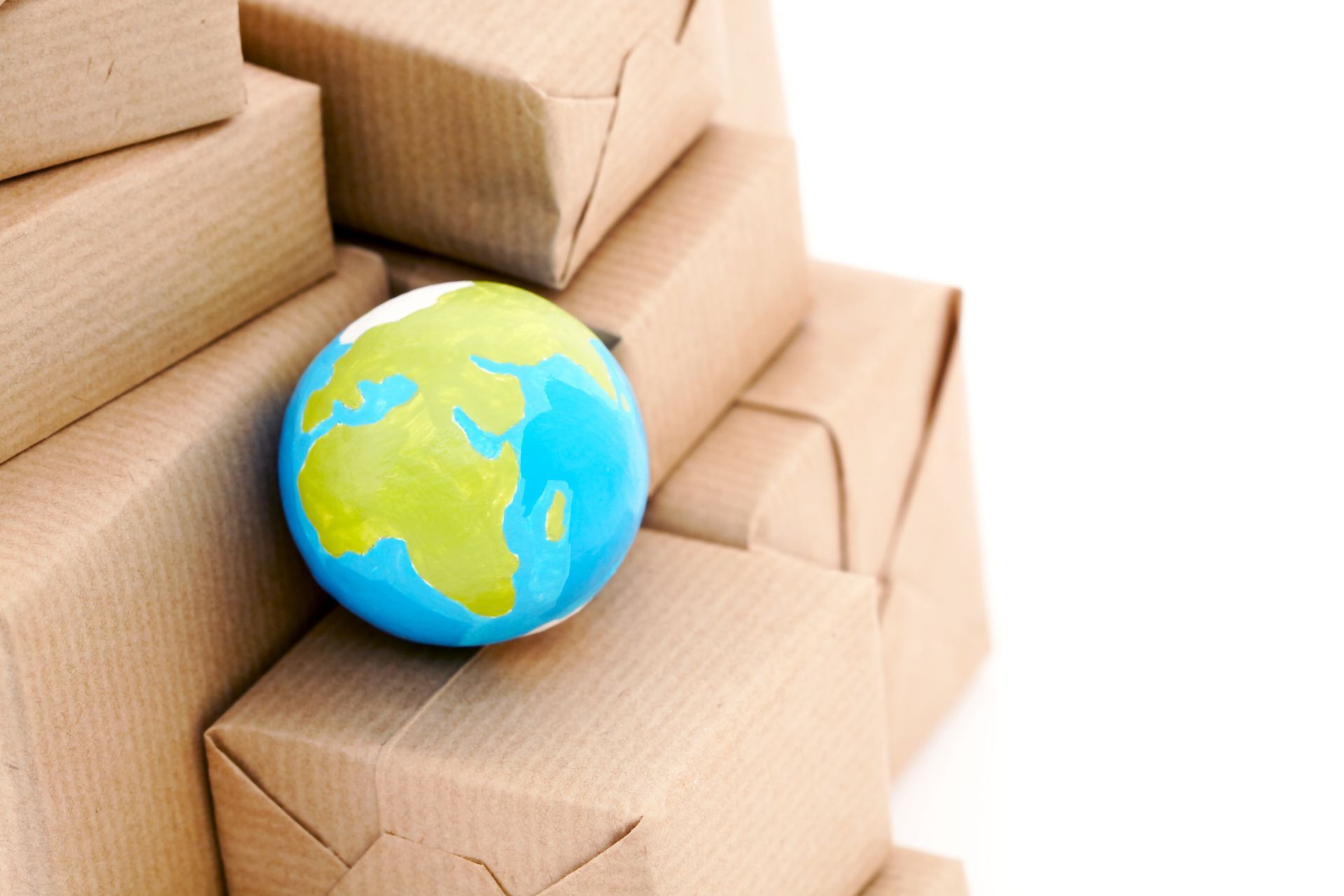 Photograph showing a small globe resting on a stack of brown cardboard boxes, symbolizing global shipping or international logistics. Photograph showing a small globe resting on a stack of brown cardboard boxes, symbolizing global shipping or international logistics.