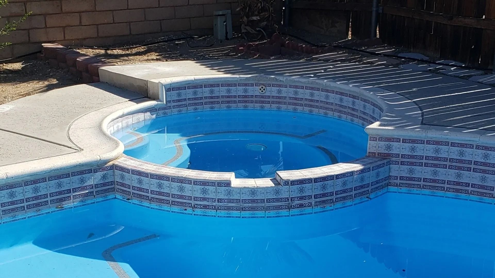 Backyard swimming pool with a raised spa, blue water, and tiled coping in sunlight