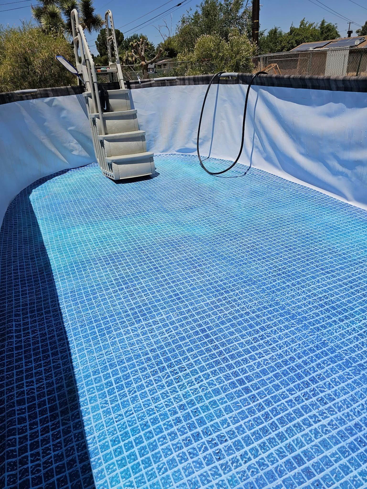 Empty above-ground pool with blue liner and a small stair ladder in sunlight