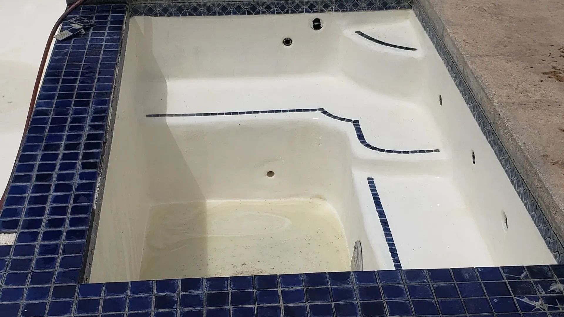 Empty white tiled pool or spa with blue tile border and built-in steps