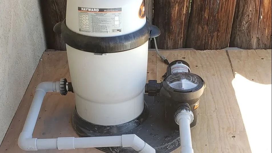 White pool pump and filtration system on a wooden deck with white PVC pipes attached