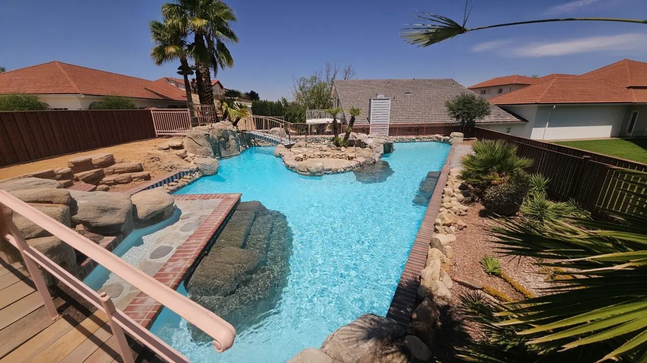 Backyard pool with rock waterfall, slide, and palm trees in a sunny residential setting