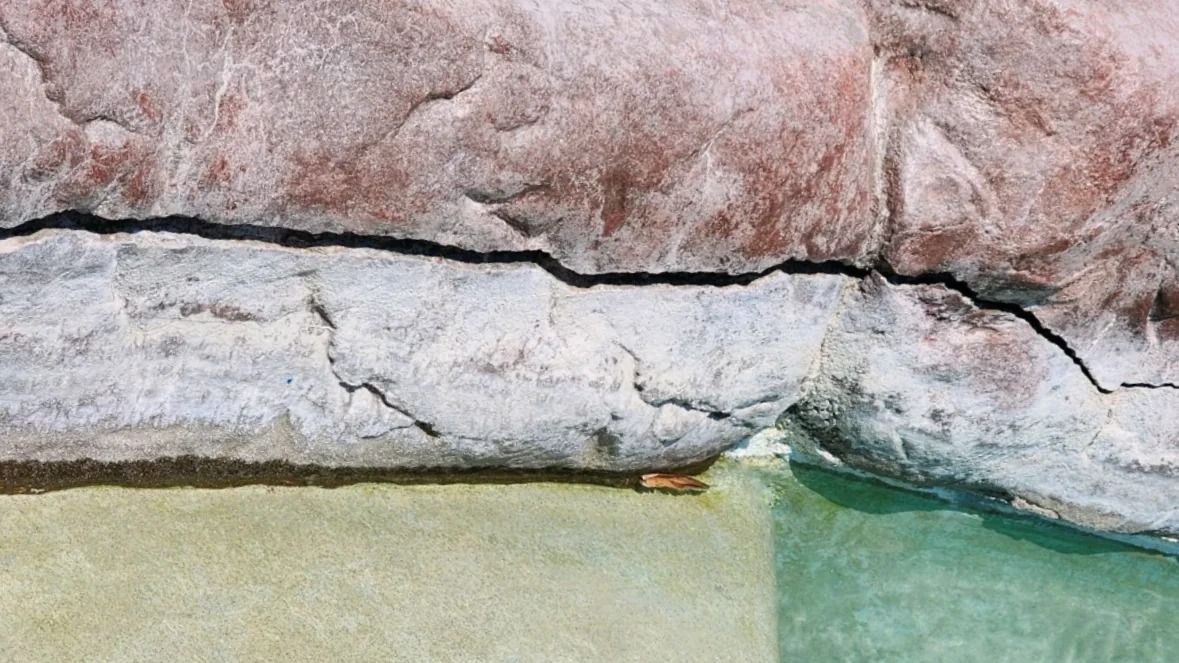 Rocky shoreline with pale stone, pink cliff, and clear green water meeting the shore