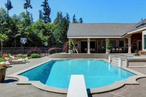 Backyard swimming pool with blue water, lounge chairs, and a patio beside a house