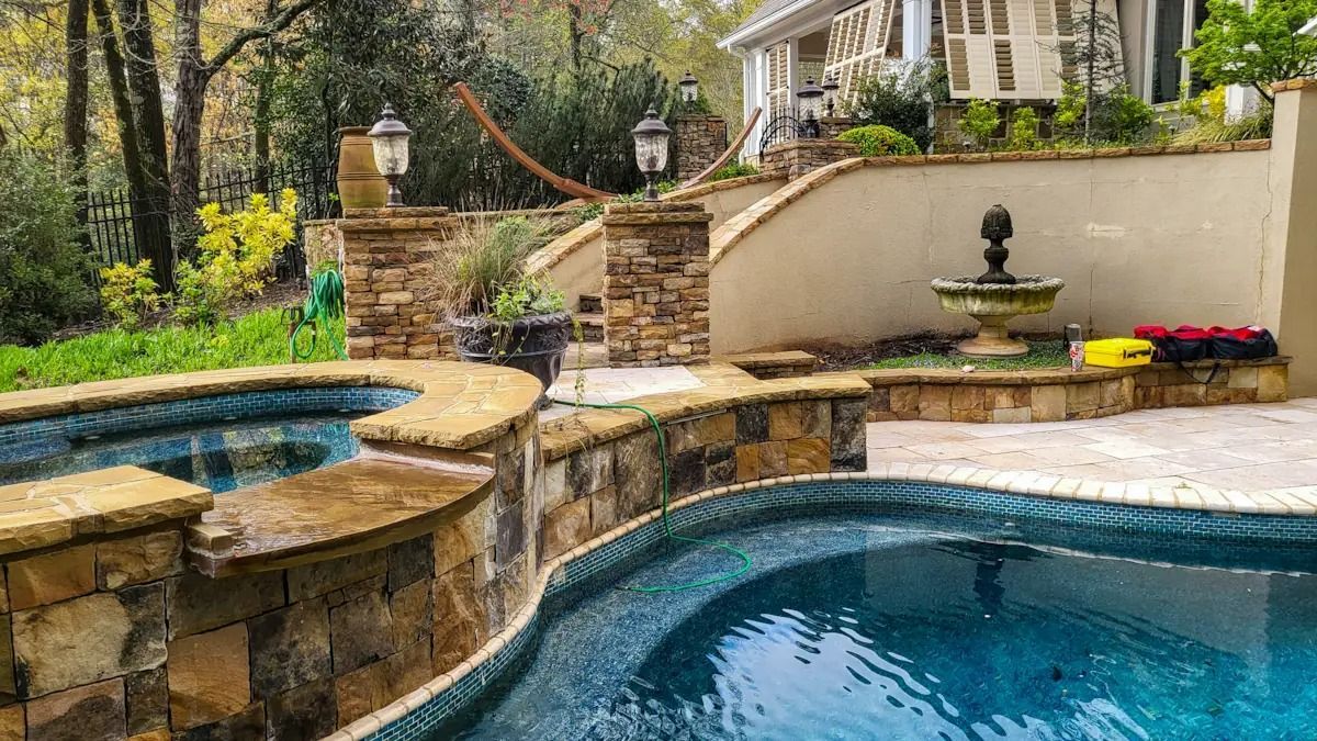 Backyard pool with stone waterfall, spa, and patio seating in a landscaped garden