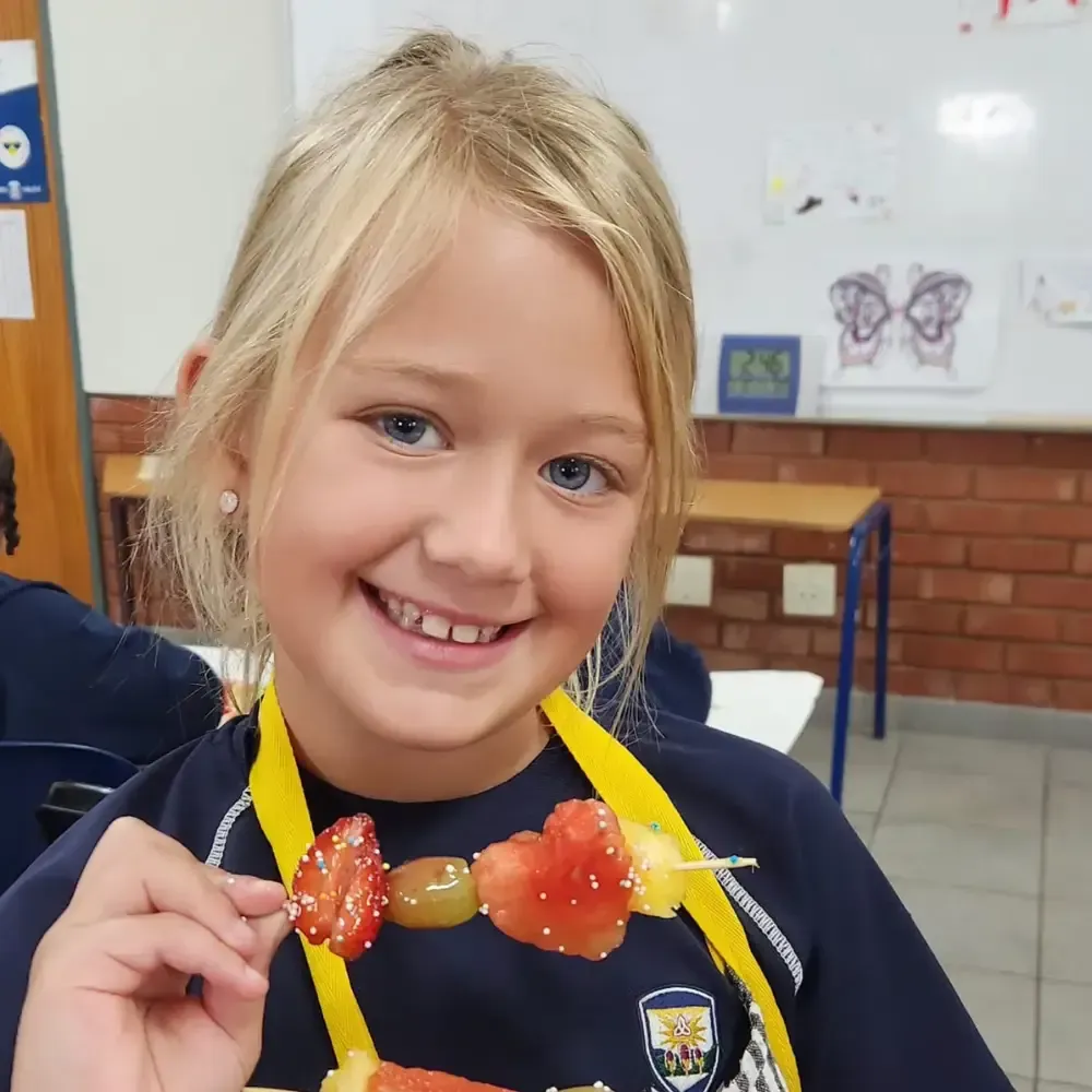 Smiling child holding a fruit snack necklace in a classroom