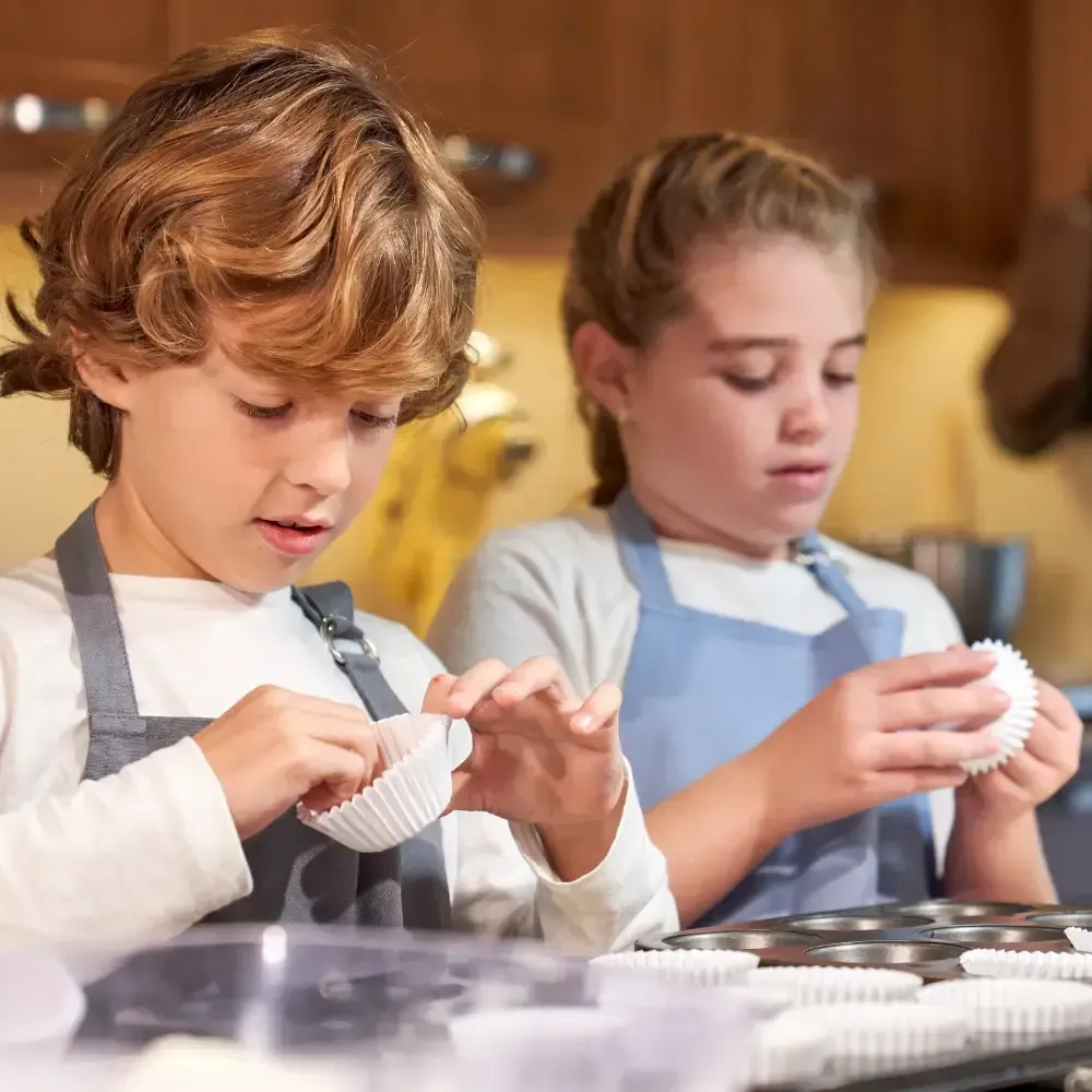 Two children in aprons decorating white baked goods in a kitchen