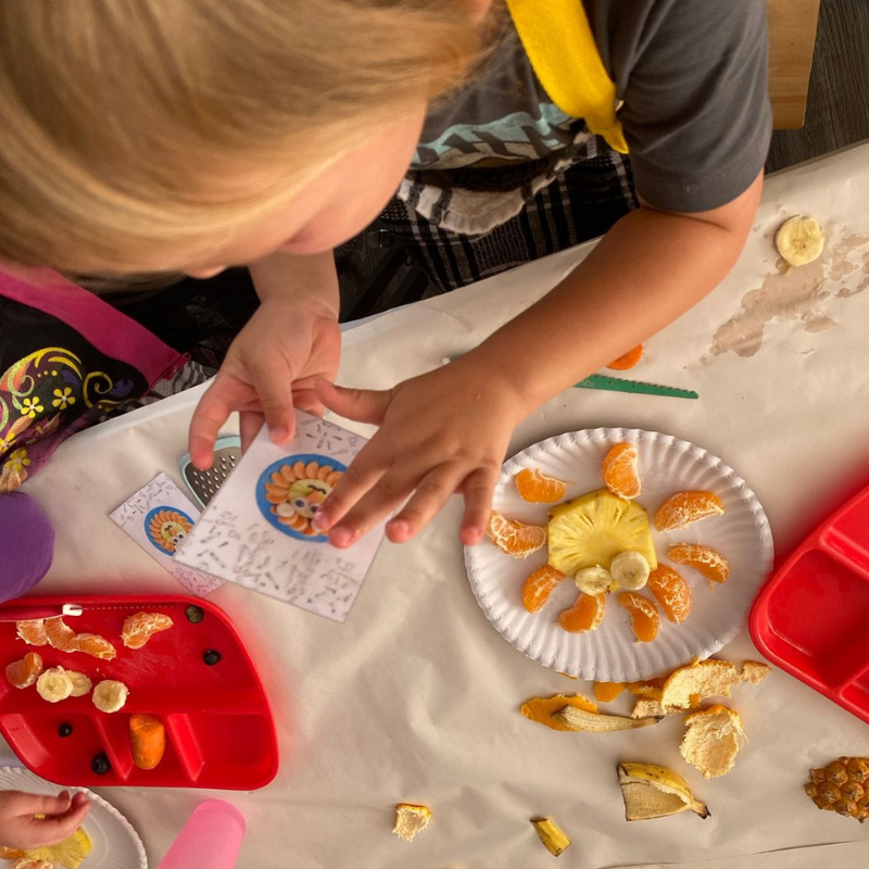 Child’s hands making a sun craft with paper plate, crayons, and cutout pieces on a table