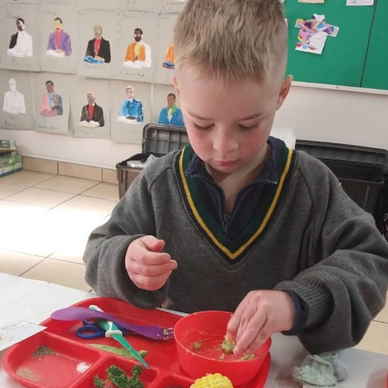 Child in a classroom using a red tray and bowl to sort small objects at a table.