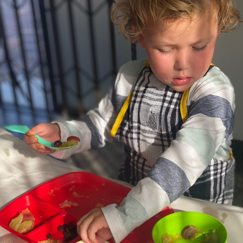 Child serving food from a red bowl into a green bowl on a sunny patio