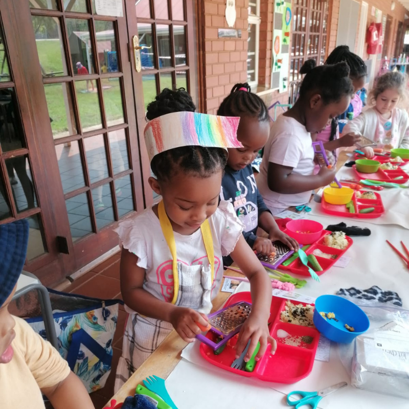 Children painting at a long table with colorful art supplies on a covered porch