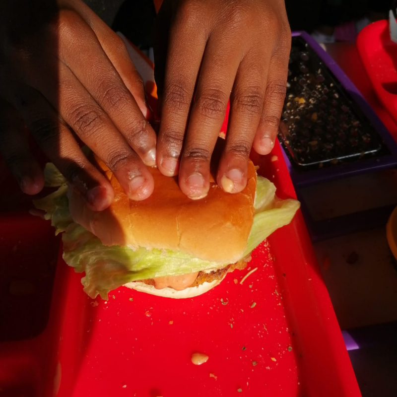 Hands holding a burger over a red tray in warm light