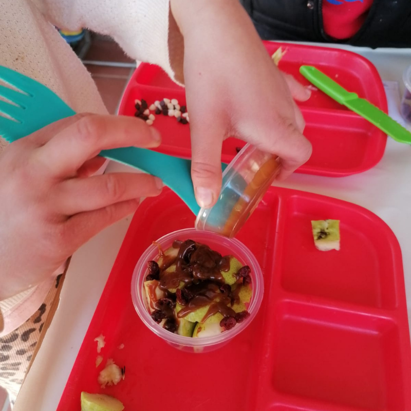 Children’s hands mixing toppings in red lunch trays at a table