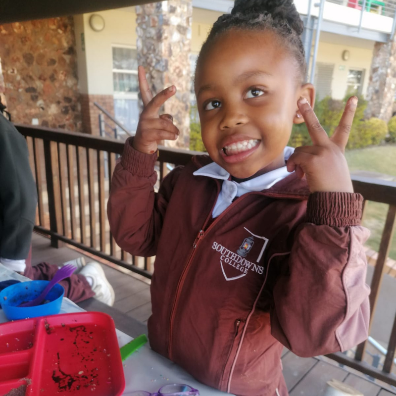 Child smiling and flashing peace signs on a porch beside colorful containers