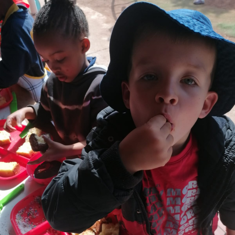 Two children eating snacks at a table; one in a blue hat looks at the camera.