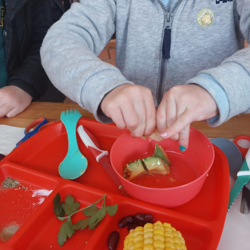 Child opening food container on a red tray with corn, berries, and parsley