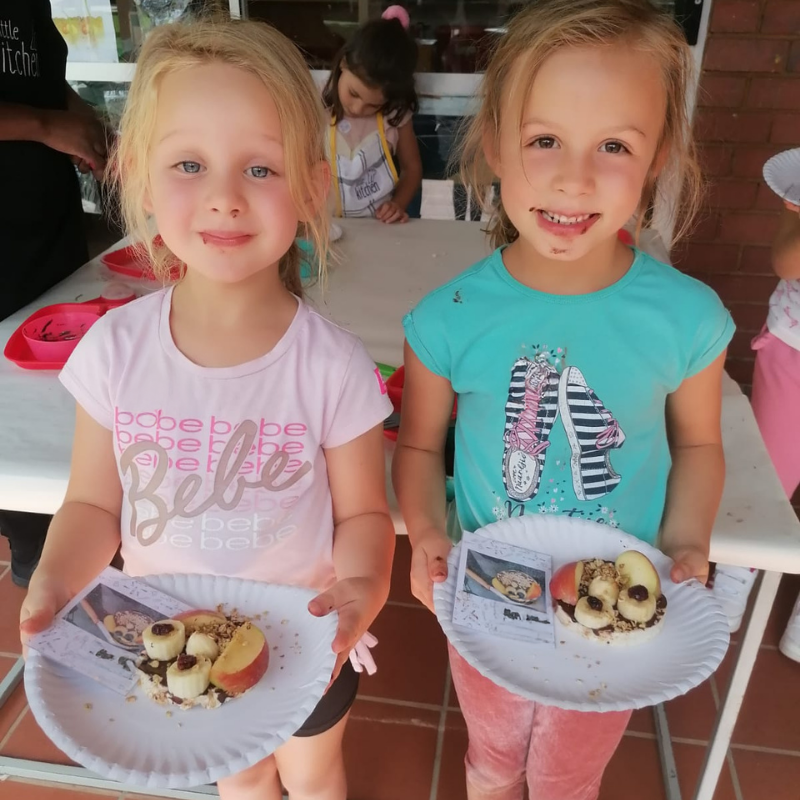 Two children holding plates with cupcakes, smiling indoors at a party table