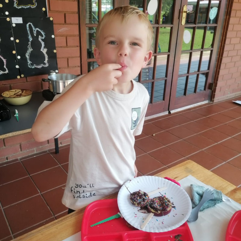 Child eating dessert at an outdoor table on a porch, with a plate and utensils in front of them.