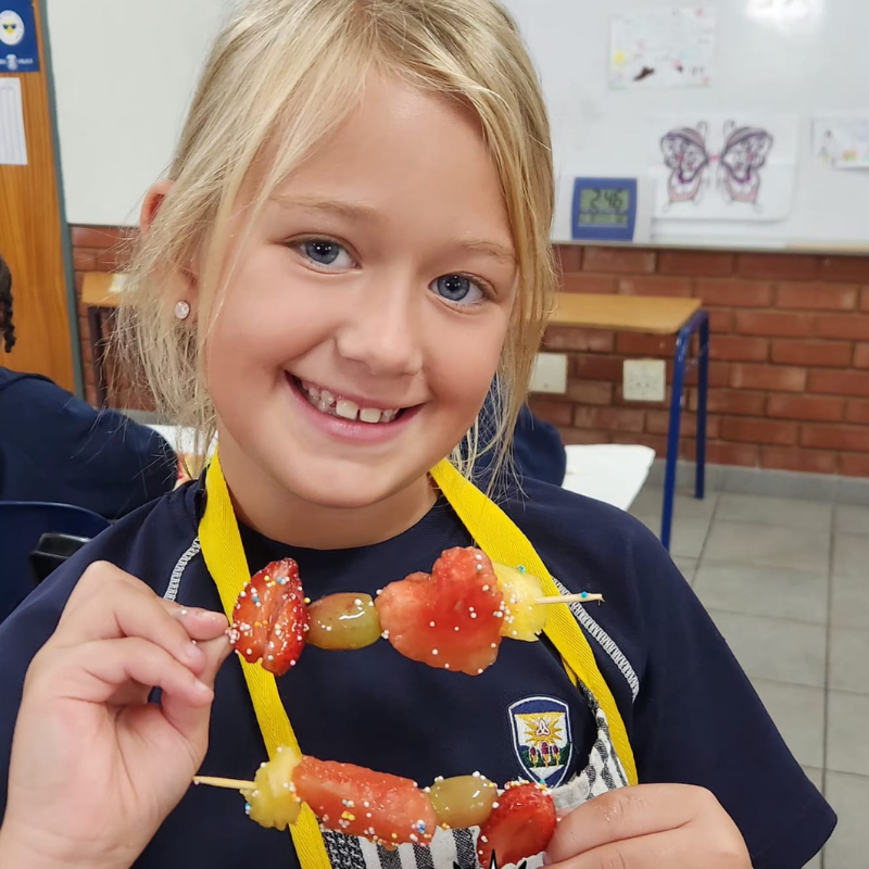 Smiling child holding a skewer of colorful fruit pieces in a classroom