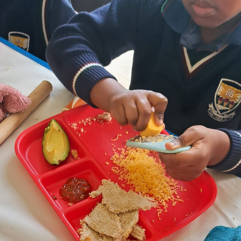 Child squeezing orange juice over a red lunch tray with fruit, toast, and jam