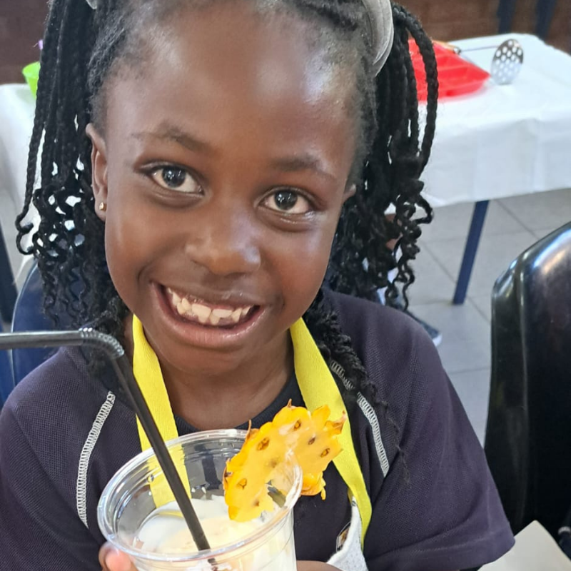 Smiling child with braids drinking from a clear cup with a pineapple slice garnish