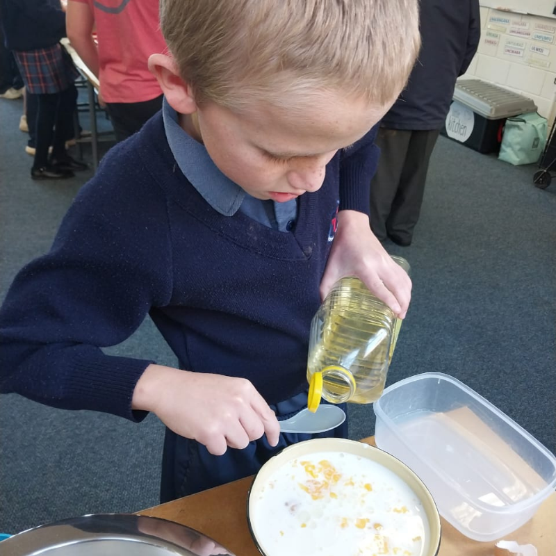 Child pouring liquid from a bottle into a spoon over a bowl at a table