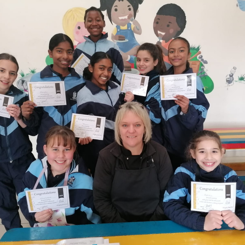 Group of students and a teacher holding certificates in a classroom, smiling at the camera.