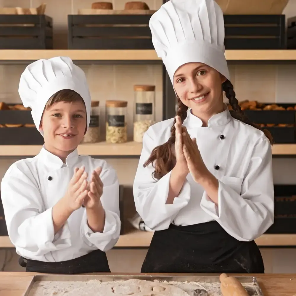Two chefs in white uniforms and hats clap beside a kitchen counter.