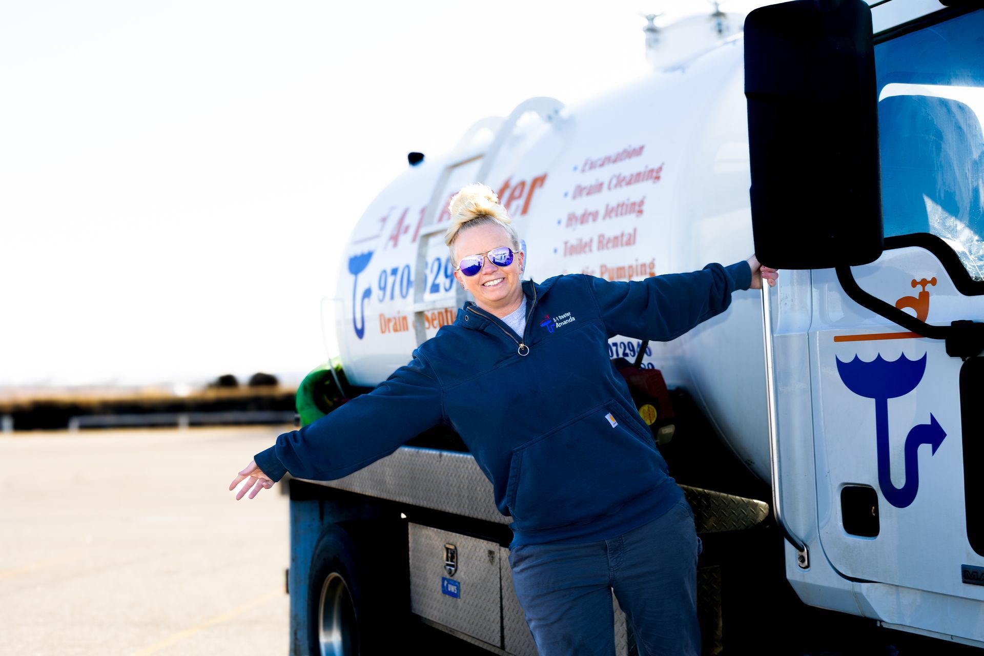 A woman is standing in front of a tanker truck with her arms outstretched.