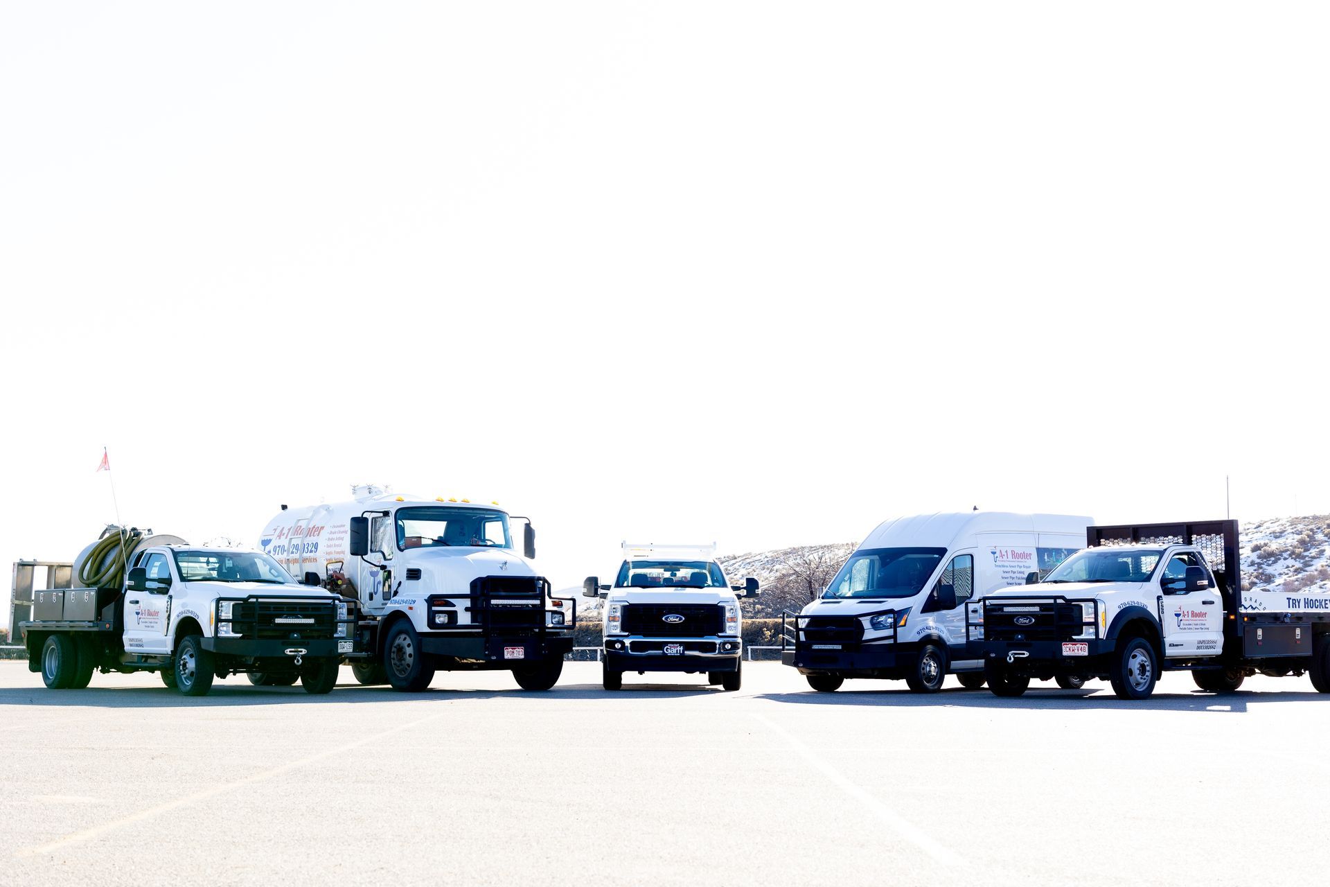 A row of white trucks and vans are parked in a parking lot.