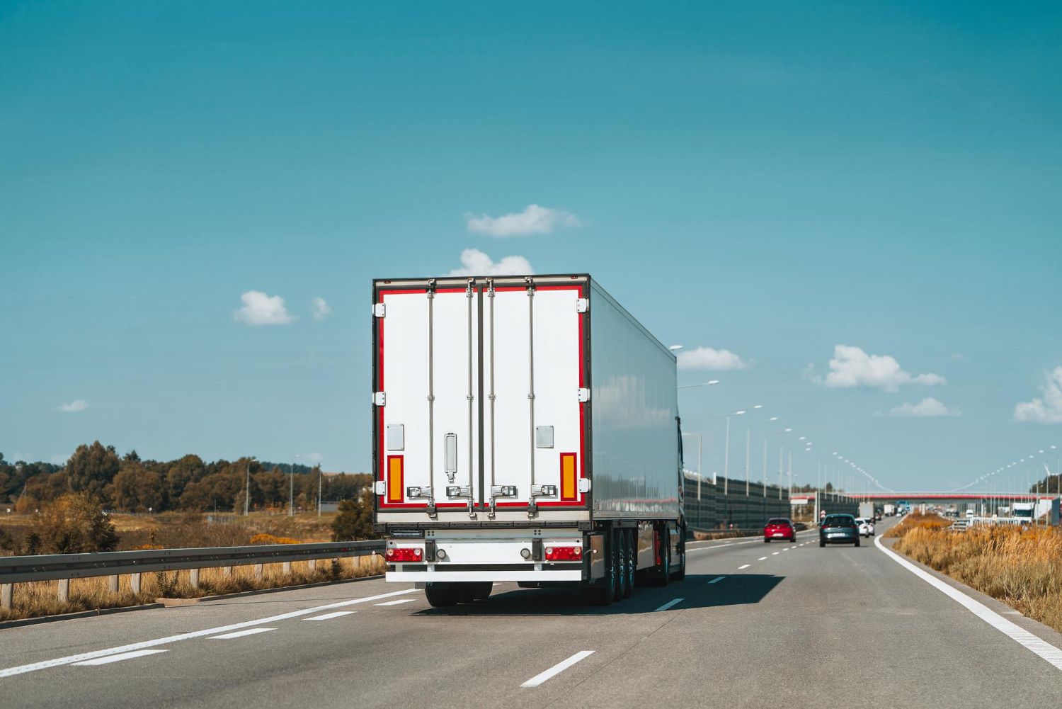 White semi-truck driving on a highway under a clear blue sky