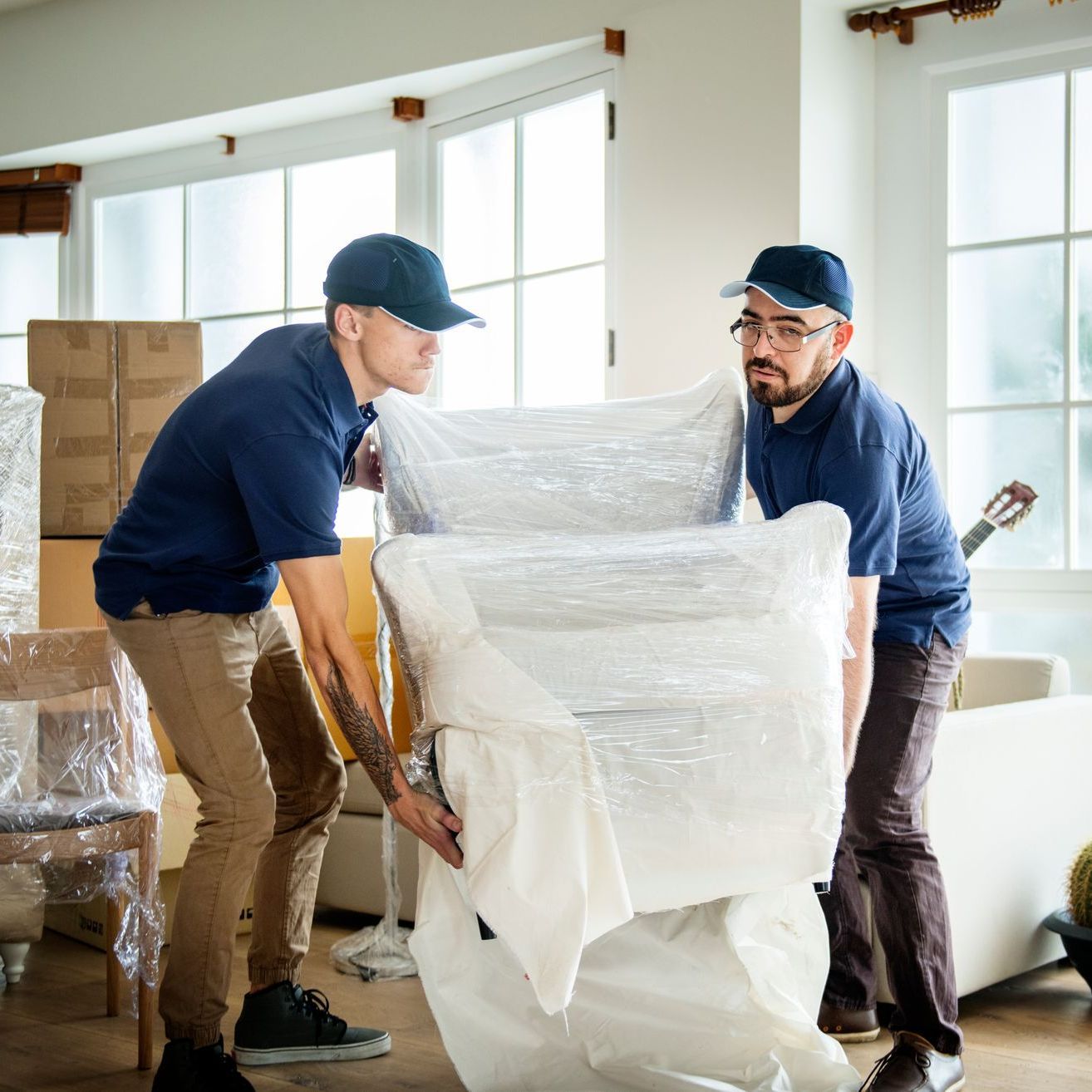 two men are wrapping a chair in plastic and one has a tattoo on his arm