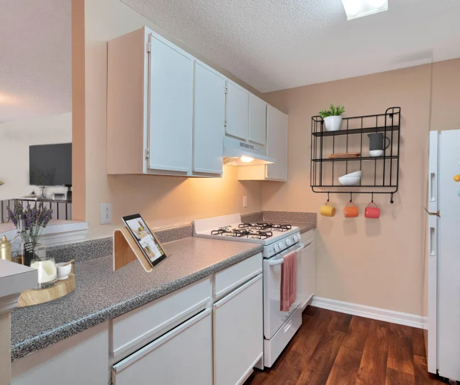 A kitchen with white cabinets, speckled countertops, a white stove, and a wall-mounted wire shelf with mugs and decor.