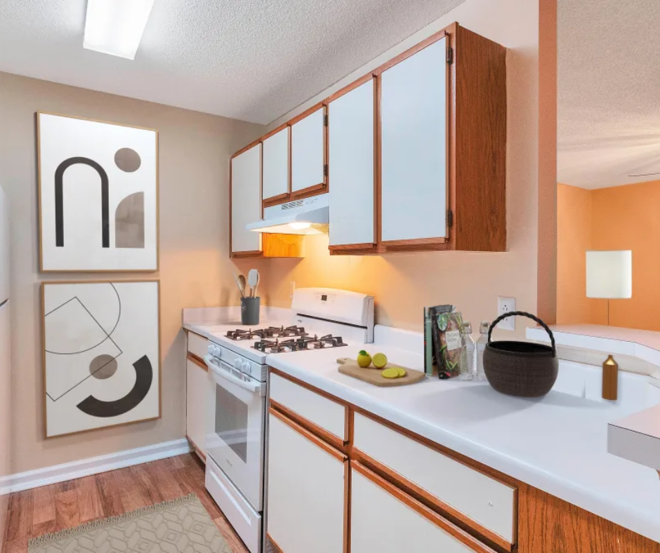 A compact kitchen with white cabinets, light-colored walls, a stove, and two abstract art prints on the wall.