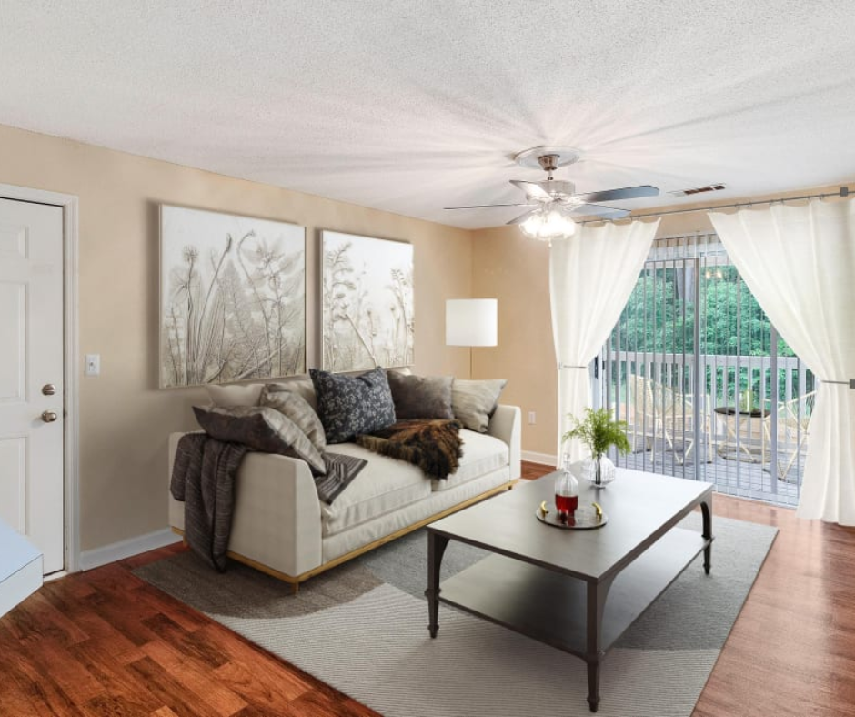 A light-colored sofa with pillows and a coffee table sit in a living room with wood floors and a balcony view.