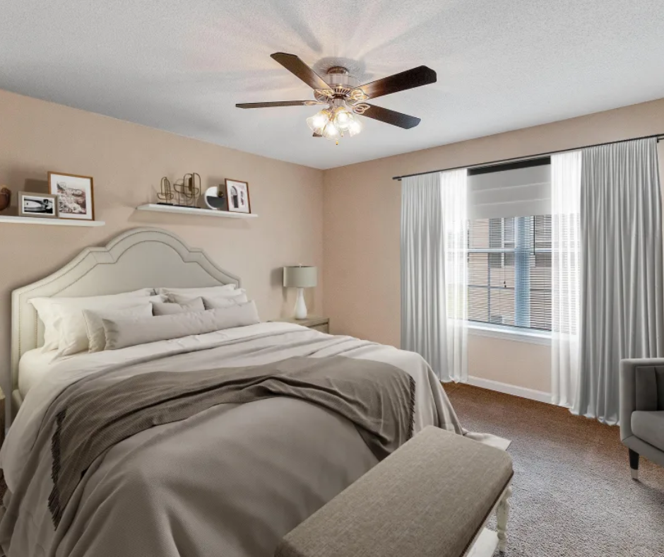 A neutral-toned bedroom with a queen bed, a white headboard, a ceiling fan, and white curtains covering a large window.