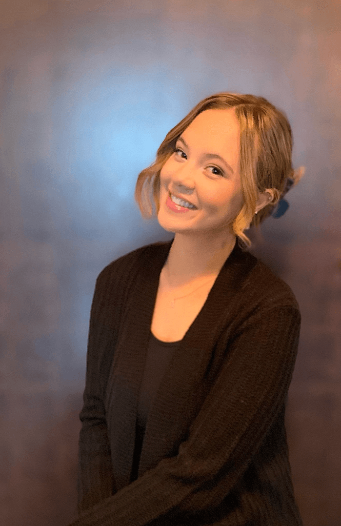 Smiling woman in a black cardigan against a soft blue-gray studio backdrop