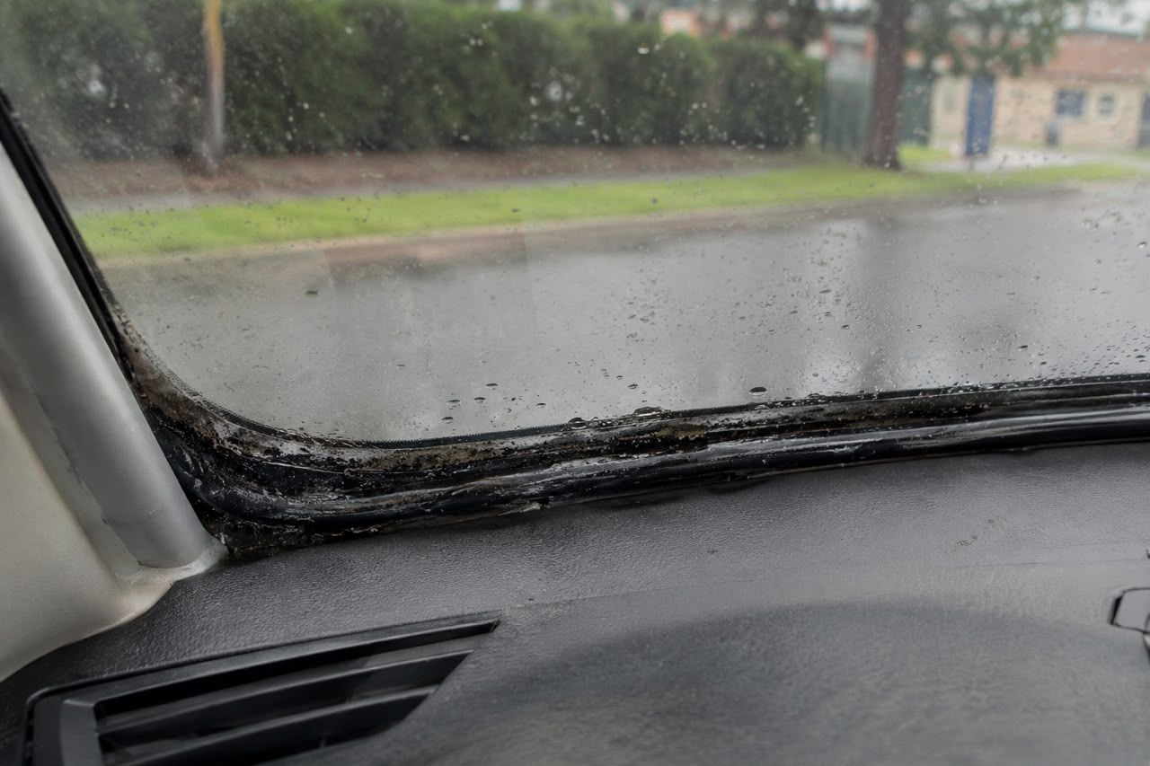 Rainy street seen through a car windshield with raindrops and dashboard in the foreground