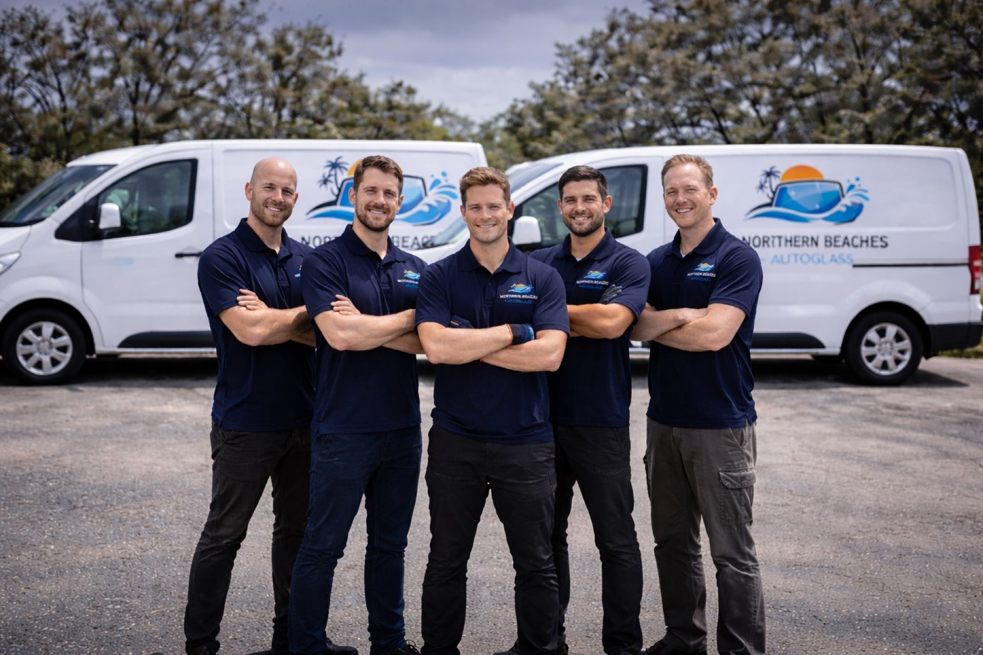 Five men in blue shirts with arms crossed in front of two company vans. 