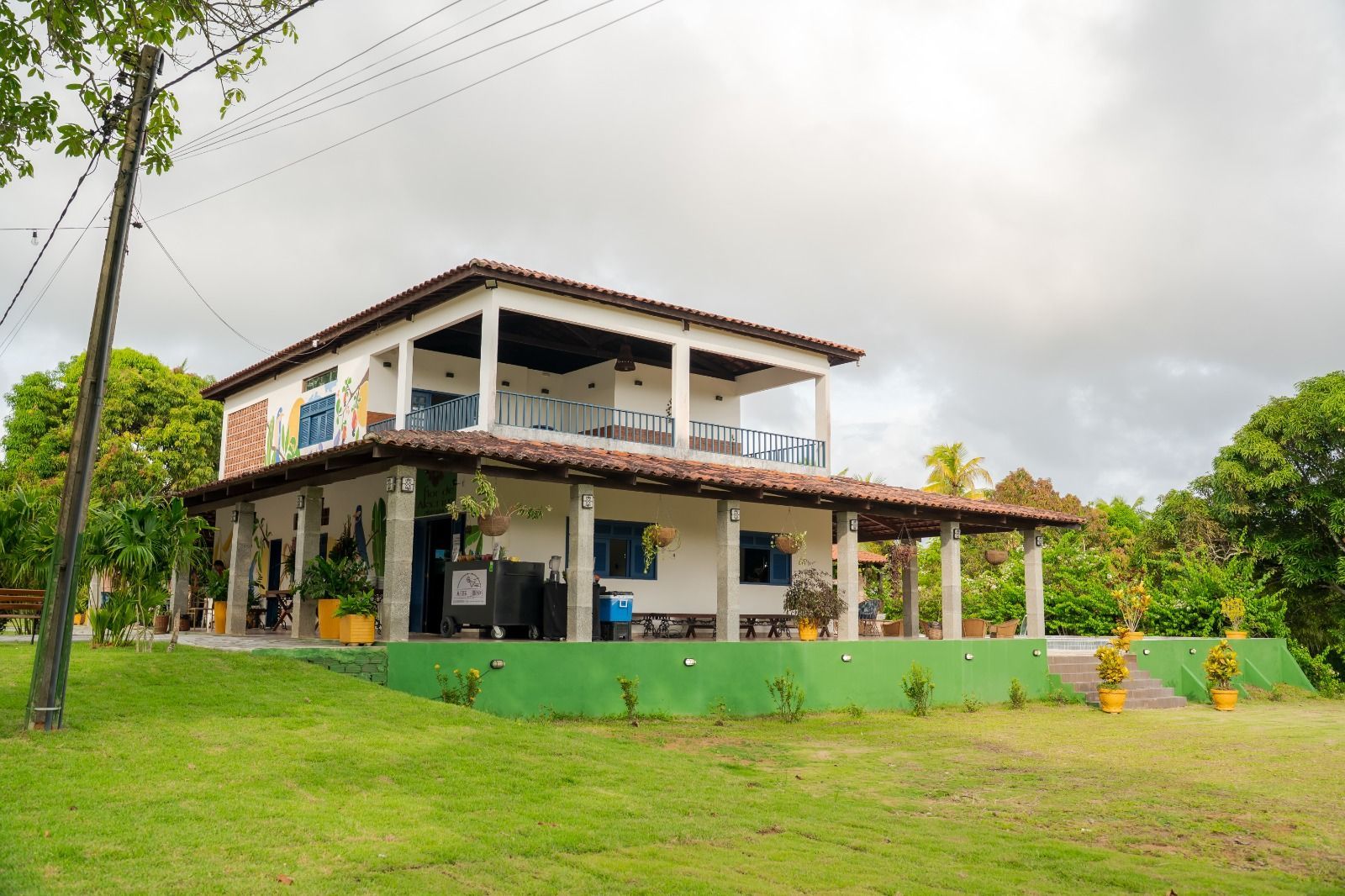 Casa de dois andares com varanda coberta e gramado verde sob um céu nublado.