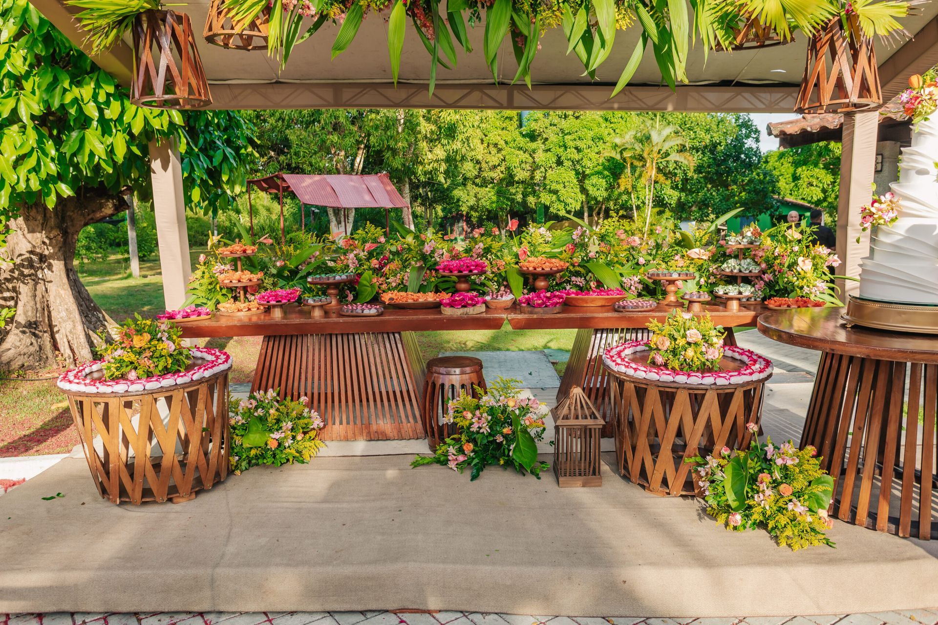 Exposição de flores tropicais com flores cor-de-rosa e vegetação exuberante sob um pavilhão de madeira sombreado.