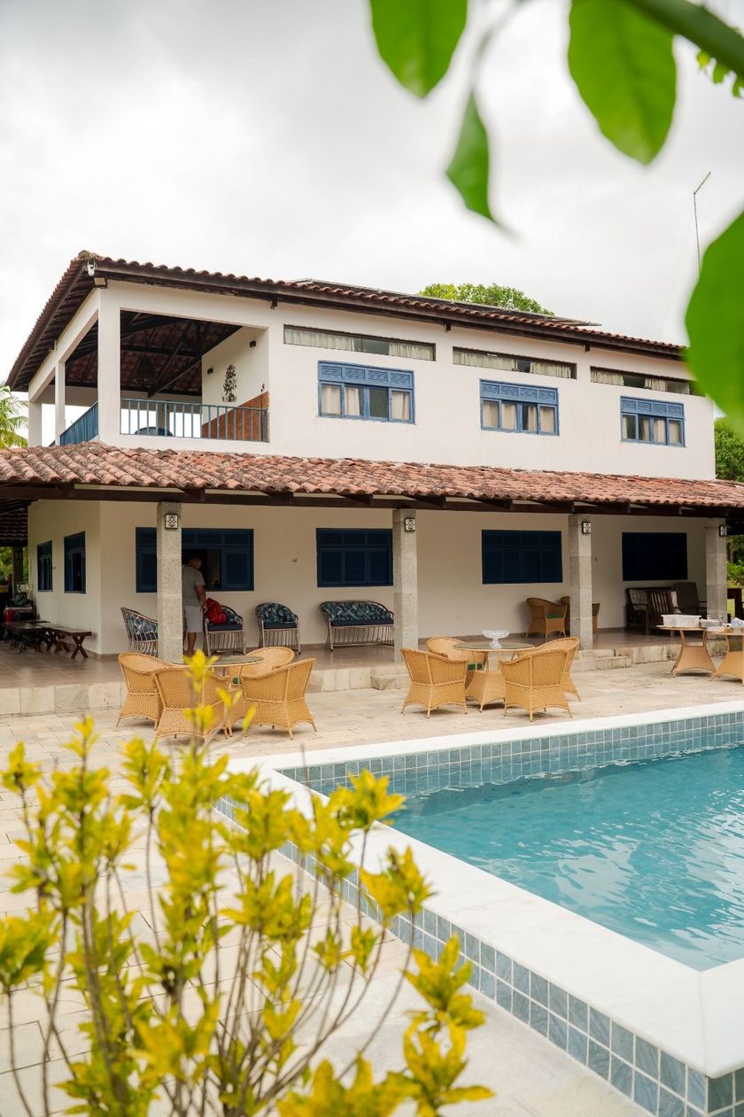 Moradia de dois andares com piscina turquesa, área de estar no pátio e plantas floridas na frente.