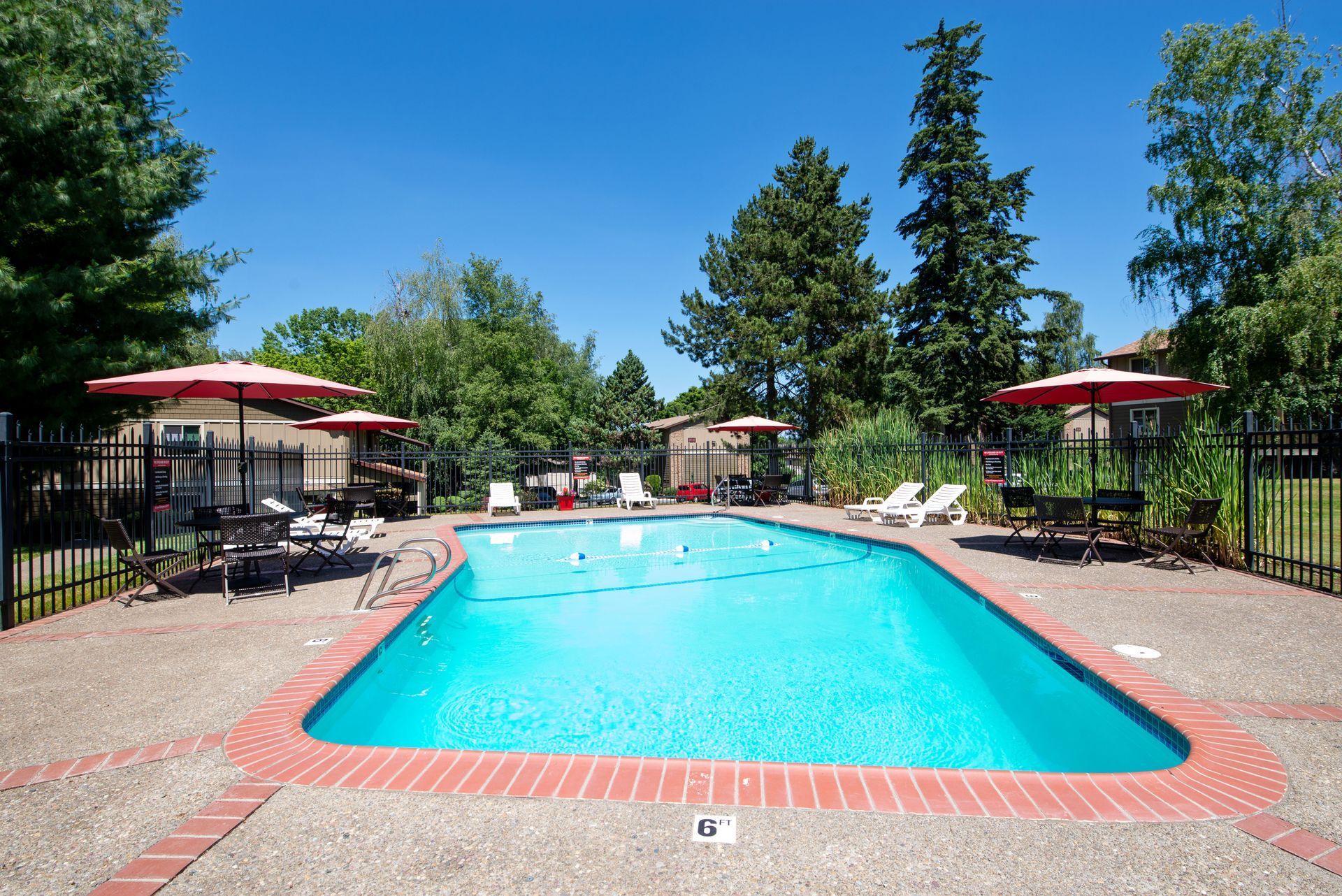 Outdoor swimming pool with lounge chairs, red umbrellas, and trees on a sunny day